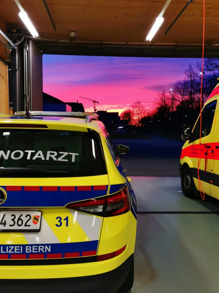 Notarztfahrzeug und Rettungswagen der Polizei Bern stehen in Garage bei Sonnenaufgang, Einsatzbereitschaft des Rettungsdienstes.