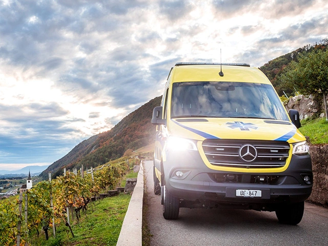 Rettungswagen fährt durch Weinberge am Bielersee bei Sonnenaufgang, Rettungsdienst im Einsatz in ländlicher Region der Schweiz.
