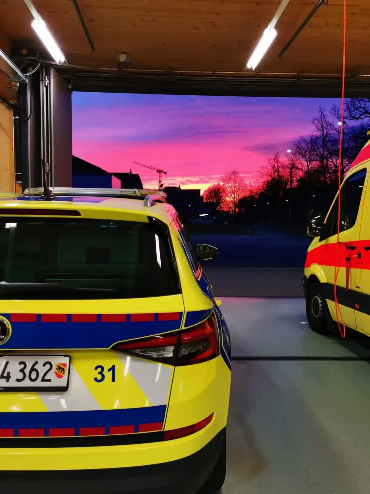 Notarztfahrzeug und Rettungswagen der Polizei Bern stehen in Garage bei Sonnenaufgang, Einsatzbereitschaft des Rettungsdienstes.